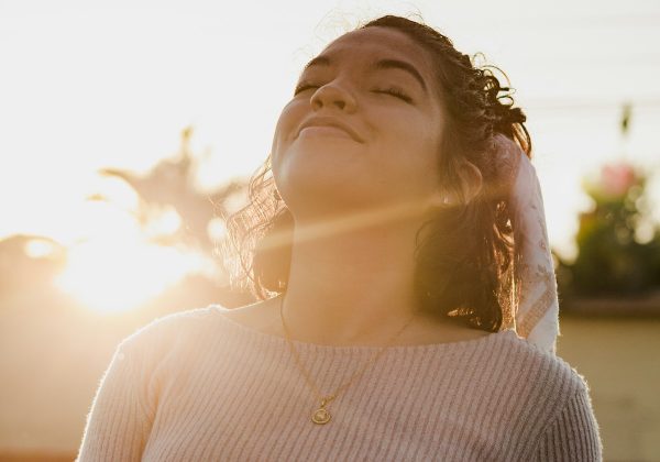 Mulher de olhos fechados respirando sob a luz do sol